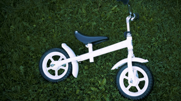 Lasten valkoinen polkupyörä kyljellään vihreällä ruohikolla