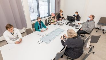 Pohjois-Karjalan hyvinvointialueen aluevaalilautakunnan kokous, valkoinen pöytä, jonka ympärillä ihmiset istuvat